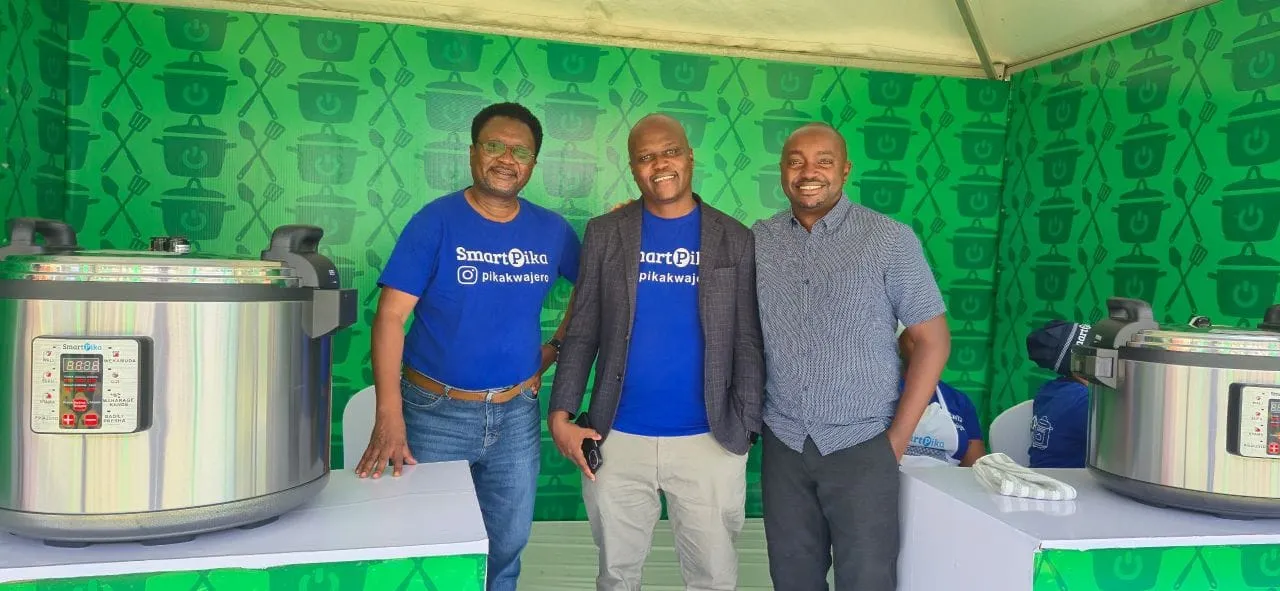 Three men smiling in front of electric pressure cookers at the Pika Smart stand