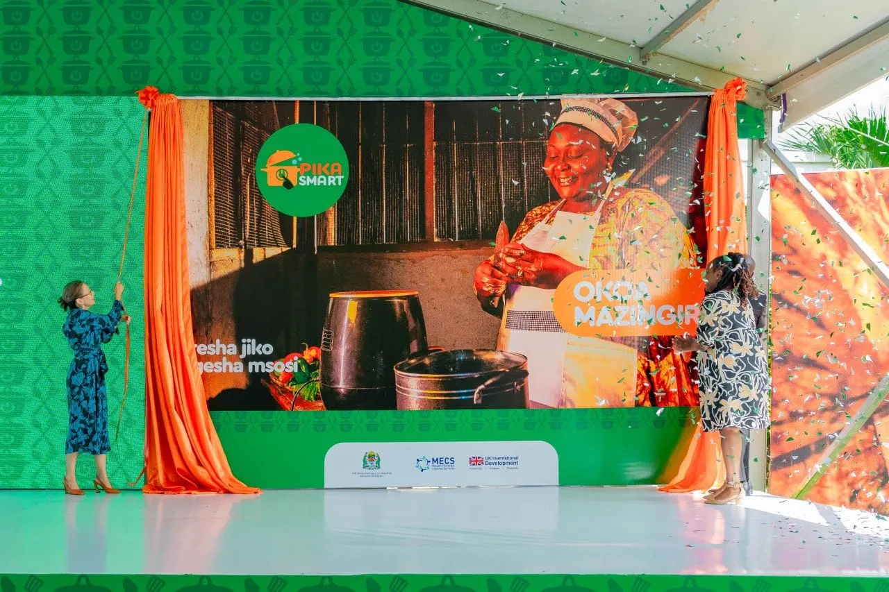 Two women unveil the Pika Smart campaign backdrop at the launch, with orange curtains and confetti